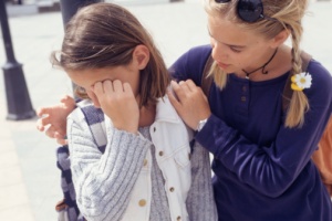 Young girl (10-11) crying, teenage girl (14-15) comforting her